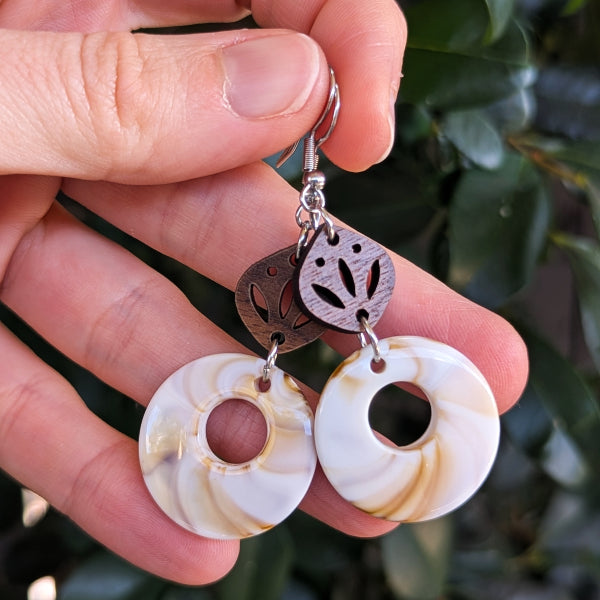 Pair of earrings with circular designs held between fingers on a leafy background