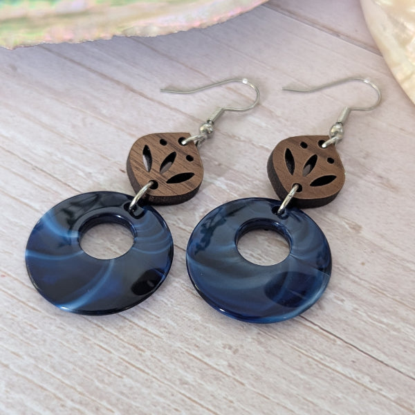 Pair of earrings with blue circular pendants and wooden leaf accents on a wooden surface.
