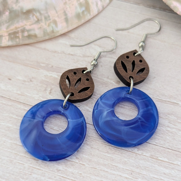 Blue circular earrings with wooden leaf accents on a light wooden surface.