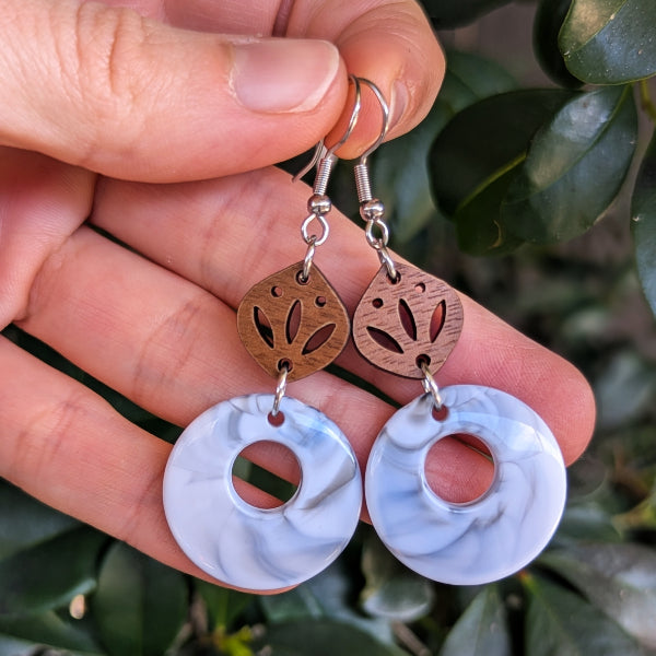 Pair of earrings with circular designs held between fingers on a leafy background