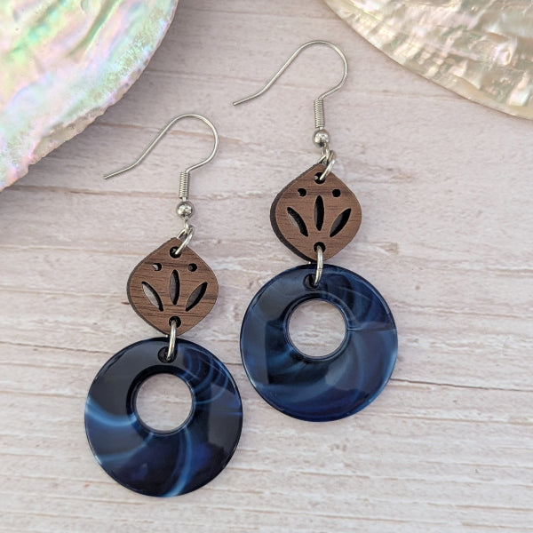 Pair of earrings with blue circular designs and brown leaf-like shapes on a wooden surface.