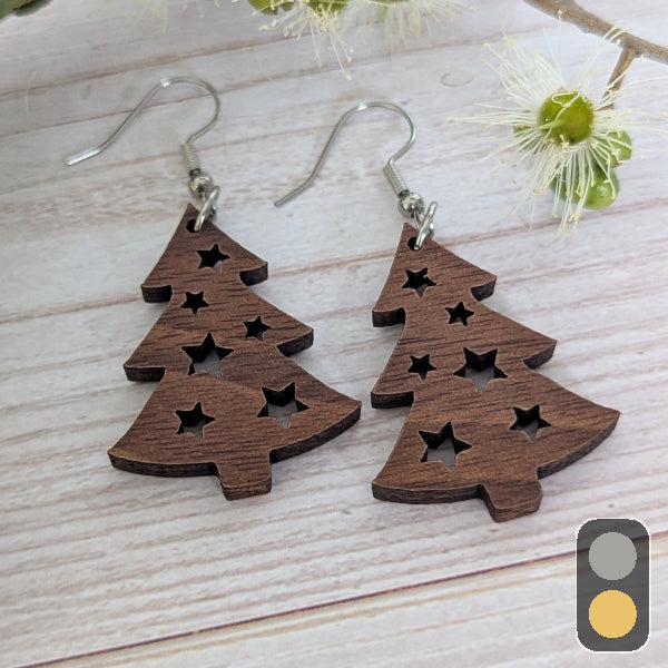 Wooden Christmas tree earrings on a light wooden surface with flowers in the background. Stainless steel hooks.