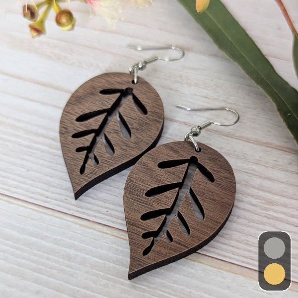 Wooden leaf-shaped earrings on a light wooden surface with blurred floral background. Stainless steel hooks.