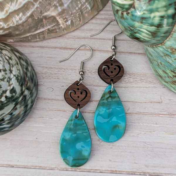 Resin turquoise coloured teardrop earrings with wooden accents on a light wood surface. Stainless steel hooks.