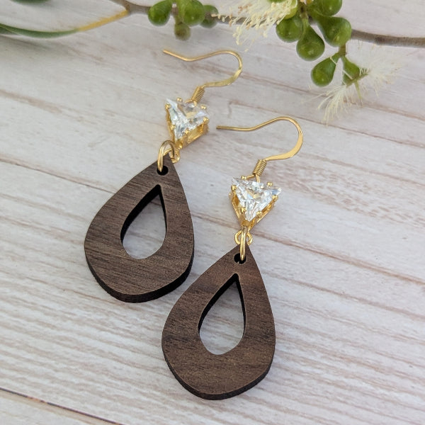 Wooden teardrop earrings with gold and crystal accents on a light wooden surface. Plated gold stainless steel hooks.