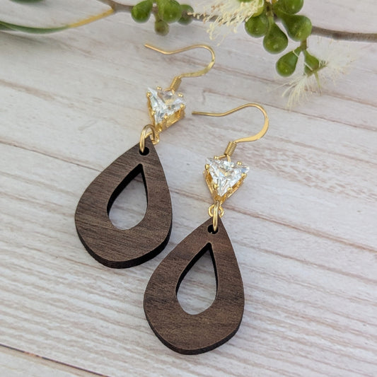 Wooden teardrop earrings with gold and crystal accents on a light wooden surface. Plated gold stainless steel hooks.