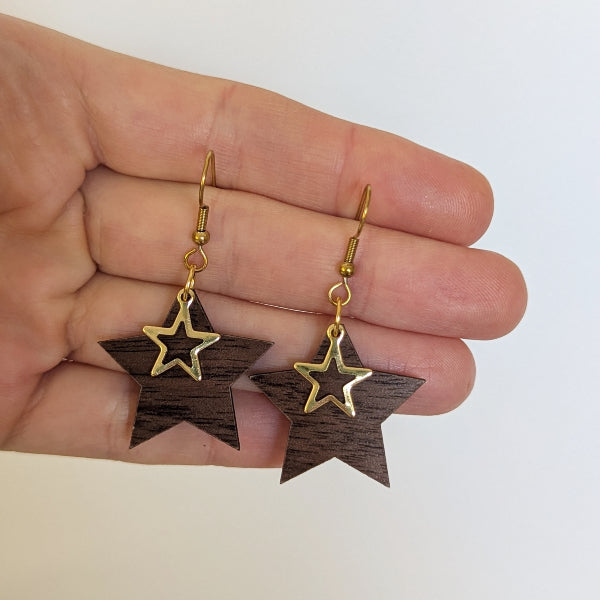 Star-shaped wooden earrings with gold accents held in a hand against a white background