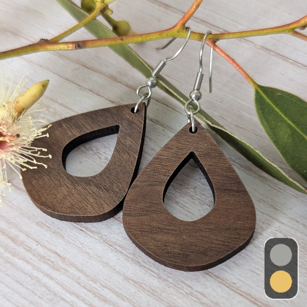 Wooden teardrop earrings on a light wooden surface with a branch and flower in the background. Stainless steel hooks.