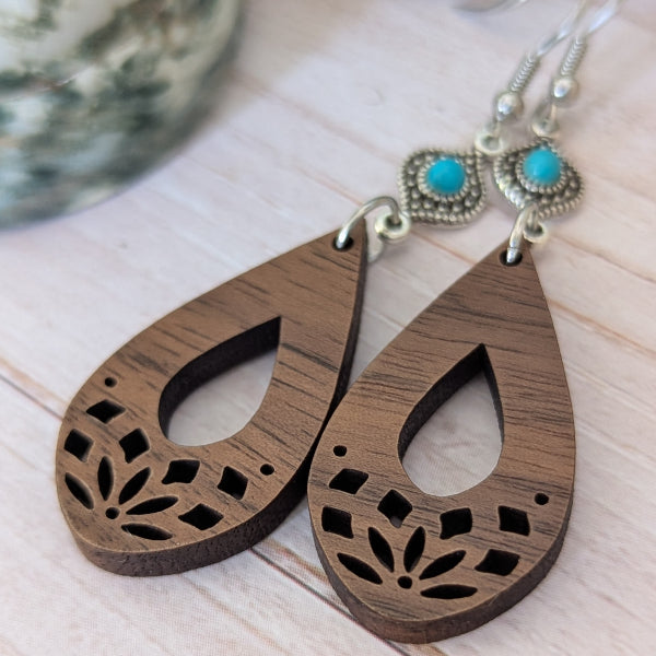 Wooden teardrop earrings with turquoise stones on a light wooden surface. Stainless steel hooks.