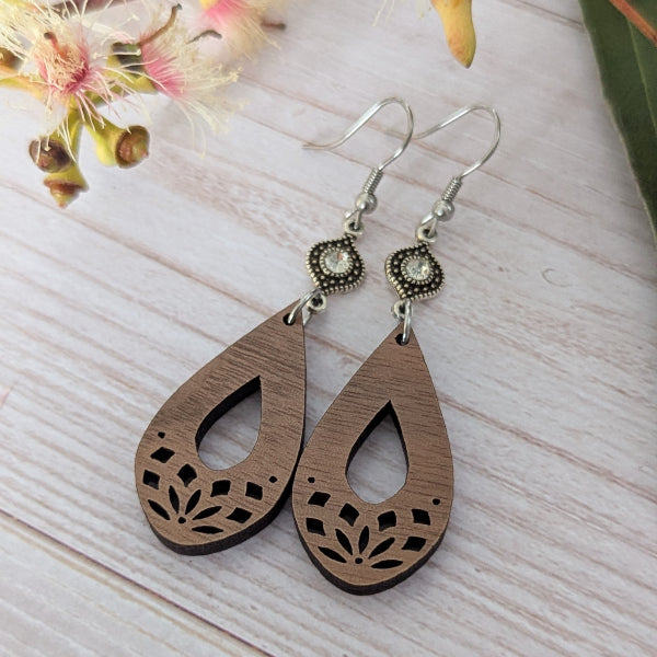 Wooden teardrop earrings with silver toned connectors with crystals, stainless steel hooks on a light wooden surface.