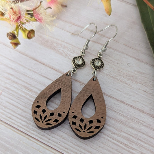 Wooden teardrop earrings with silver toned connectors with crystals, stainless steel hooks on a light wooden surface.