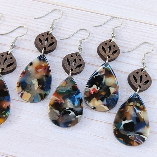 Pairs of earrings with teardrop-shaped colorful drops and wooden tops on a light wood background.