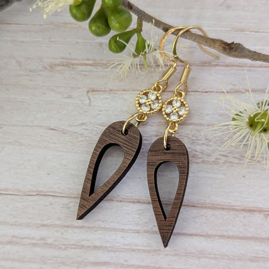 Wooden drop earrings with gold and crystal accents on a light wooden surface. Plated gold stainless steel hooks.