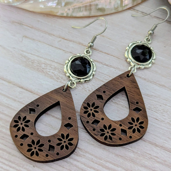 Wooden teardrop earrings with black stones on a light wooden surface