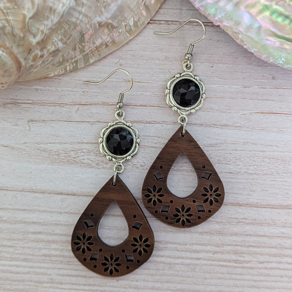 Wooden teardrop earrings with black stones on a wooden surface