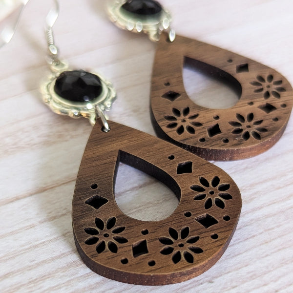 Wooden earrings with floral cutouts on a light wooden surface