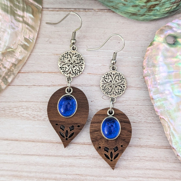 Wooden earrings with blue stones and silver floral elements on a wooden surface.