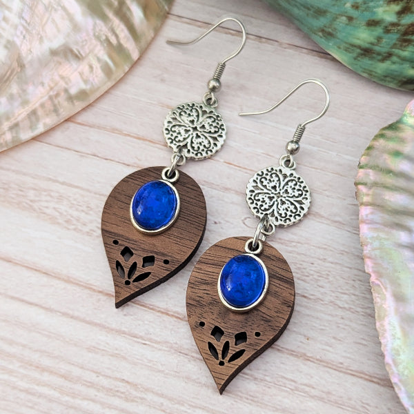 Wooden earrings with blue stones and stainless steel hooks on a light wooden surface.