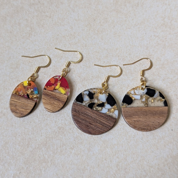Two pairs of colourful earrings made from resin and wood on a beige background. Plated gold hooks.