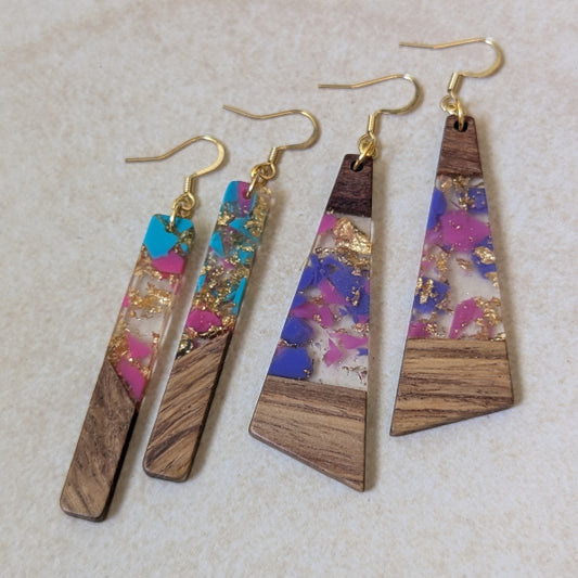 Two pairs of colourful earrings made from resin and wood on a beige background. Plated gold hooks.