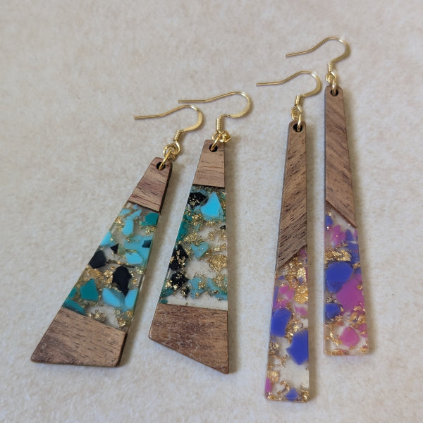 Two pairs of colourful earrings made from resin and wood on a beige background. Plated gold hooks.