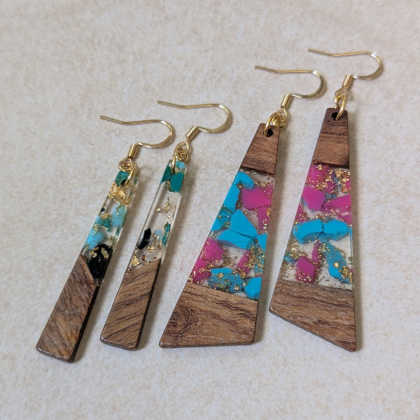 Two pairs of colourful earrings made from resin and wood on a beige background. Plated gold hooks.