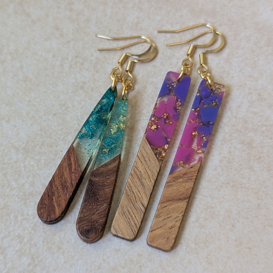 Two pairs of colourful earrings made from resin and wood on a beige background. Plated gold hooks.