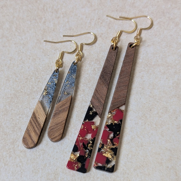 Two pairs of colourful earrings made from resin and wood on a beige background. Plated gold hooks.