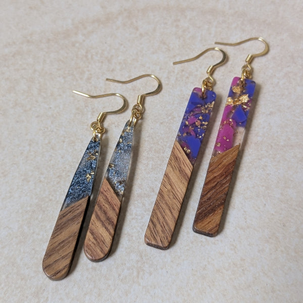 Two pairs of colourful earrings made from resin and wood on a beige background. Plated gold hooks.