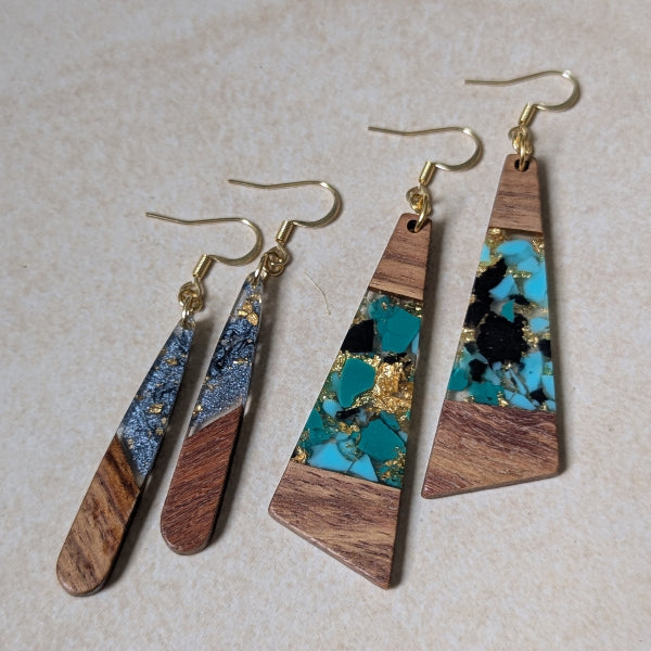 Two pairs of colourful earrings made from resin and wood on a beige background. Plated gold hooks.