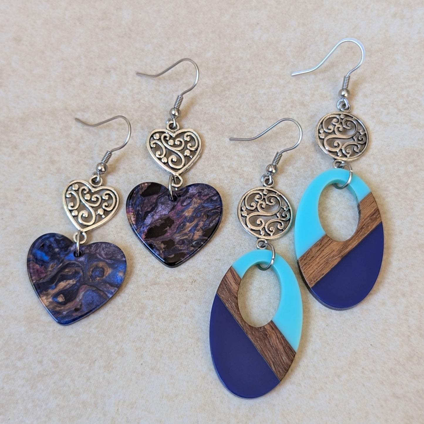 Two pairs of earrings with heart and oval designs on a beige background