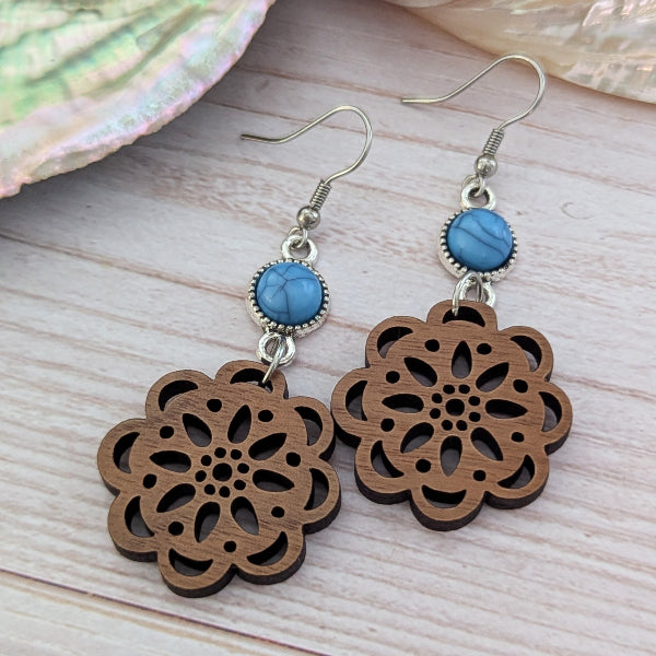 Wooden floral earrings with blue connectors on a wooden surface