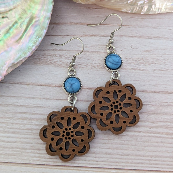 Wooden floral earrings with blue connectors on a wooden surface