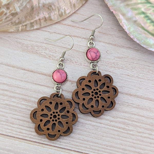 Wooden floral earrings with pink stone connectors on a wooden surface