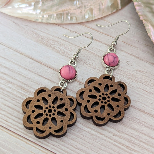 Wooden floral earrings with pink stone connectors on a wooden surface