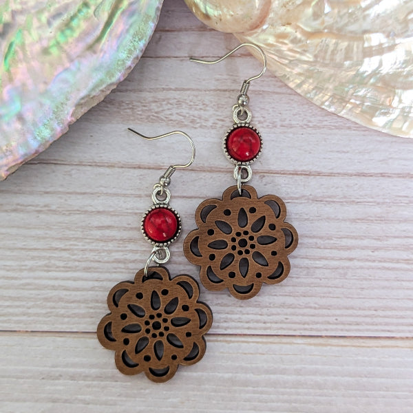 Wooden floral earrings with red stone connectors on a wooden surface
