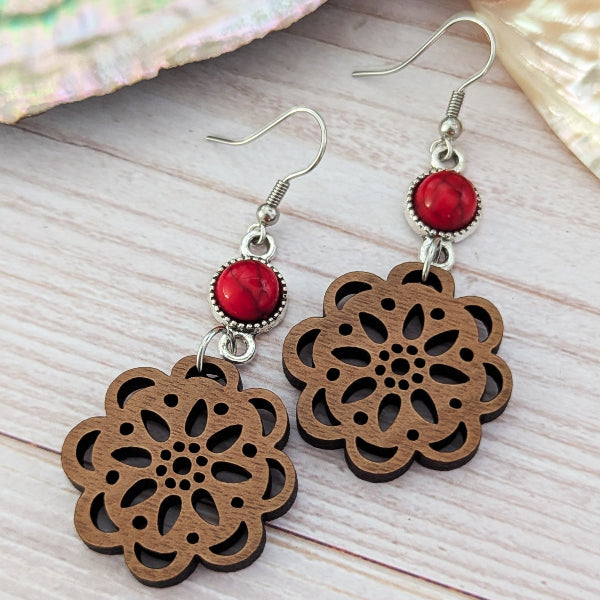 Wooden floral earrings with red stone connectors on a wooden surface
