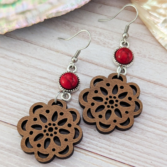 Wooden floral earrings with red stone connectors on a wooden surface