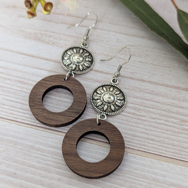 Wooden earrings with silver toned circular designs on a light wooden surface. Stainless steel hooks.