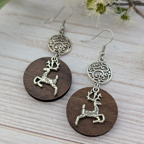 Wooden earrings with reindeer charms on a light wooden surface. Stainless steel hooks.