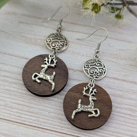 Wooden earrings with reindeer charms on a light wooden surface. Stainless steel hooks.