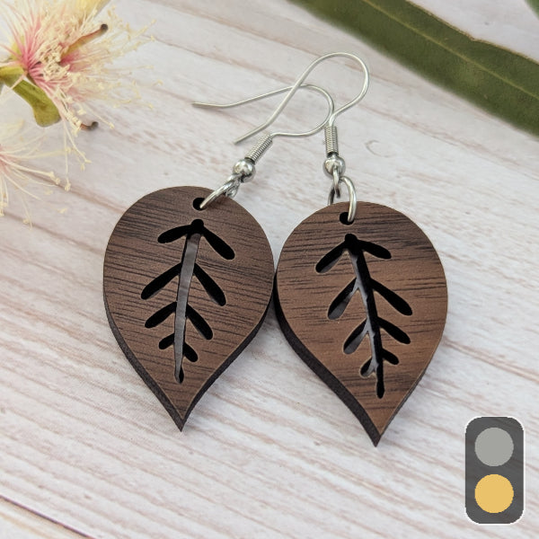 Wooden leaf-shaped earrings with cut-out designs on a light wooden surface. Stainless steel hooks.
