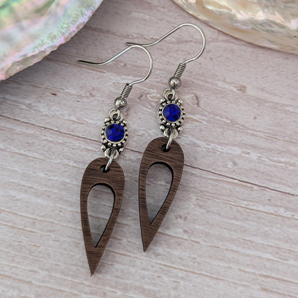 Wooden earrings with dark blue crystal connectors, light wood background. Stainless steel hooks.
