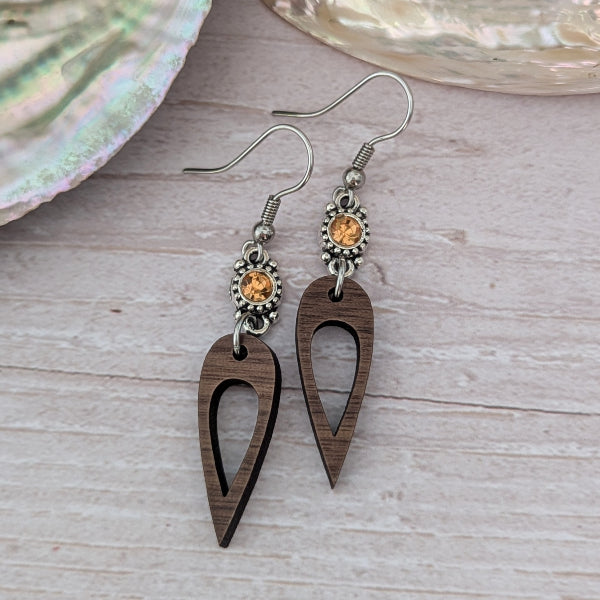 Wooden earrings with orange crystal connectors, light wood background. Stainless steel hooks.