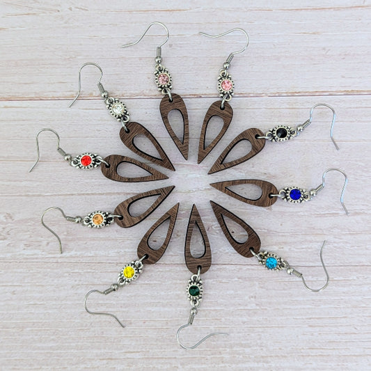 Wooden earrings with colorful gemstones arranged in a circular pattern on a light wooden surface.