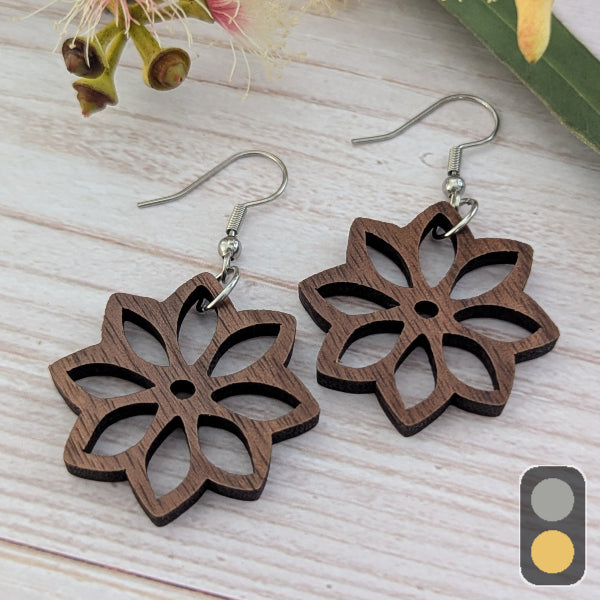 Wooden floral earrings on a light wooden surface with flowers in the background. Stainless steel hooks.