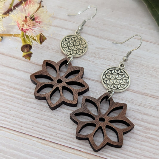 Wooden flower-shaped earrings with silver floral designs on a light wooden surface. Stainless steel hooks.