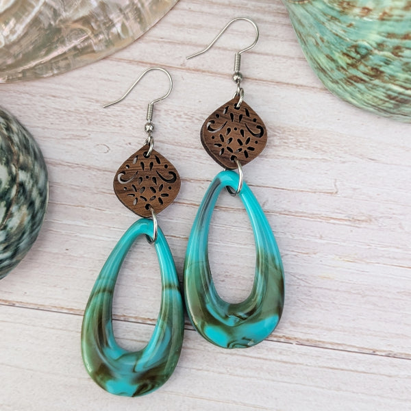 Turquoise/brown teardrop earrings with wooden floral designs on a wooden surface. Stainless steel hooks.